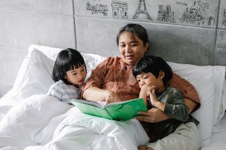 Un madre junto a sus hijos en la cama leyendo un cuento