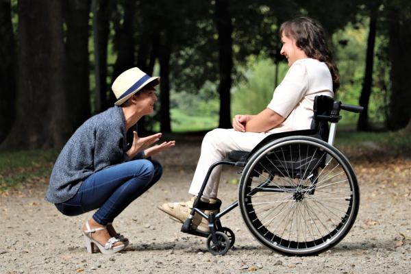 Una mujer con silla de ruedas interactúa con otra mujer en un parque